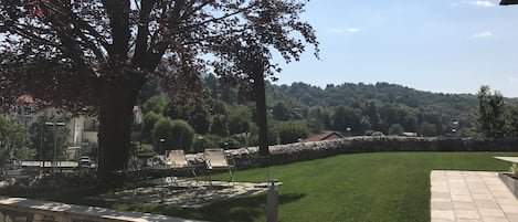 A well-maintained lawn with a stone wall and metal chairs, a large tree, and a view of a hilly landscape in the background.