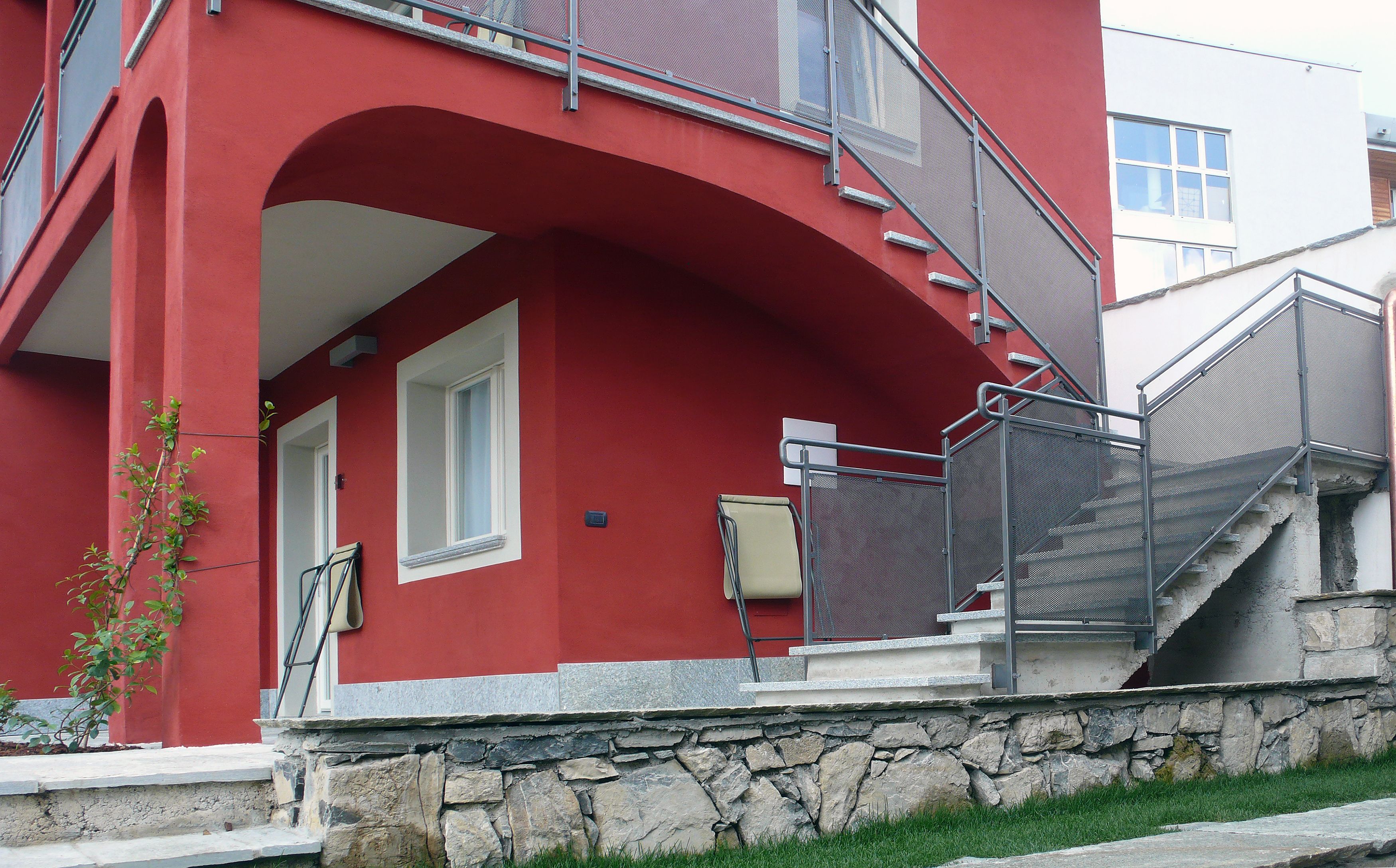 Un bâtiment rouge avec un socle en pierre, un escalier en métal et un petit balcon.
