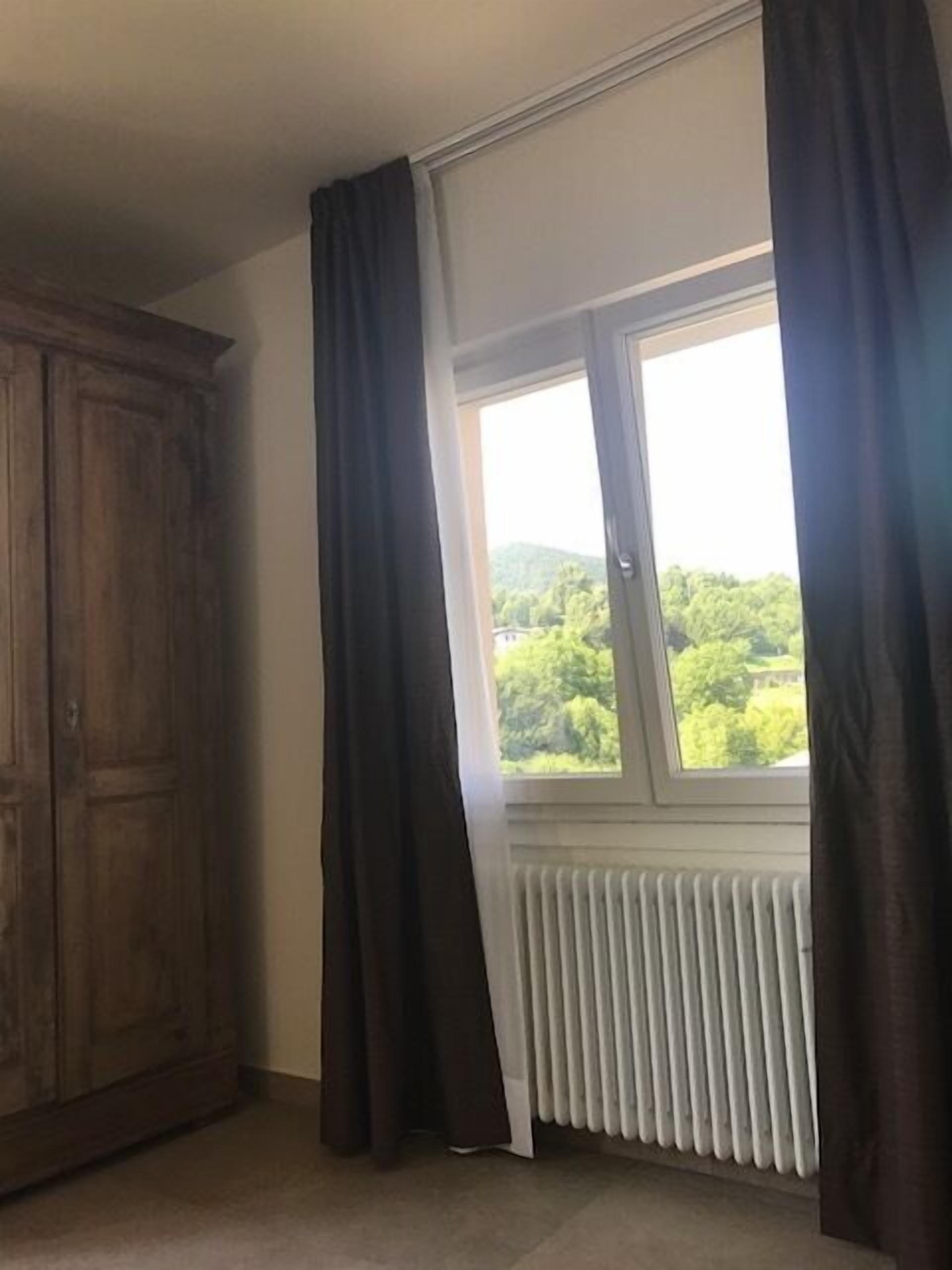 A room with a large window, a radiator, and a wooden wardrobe.