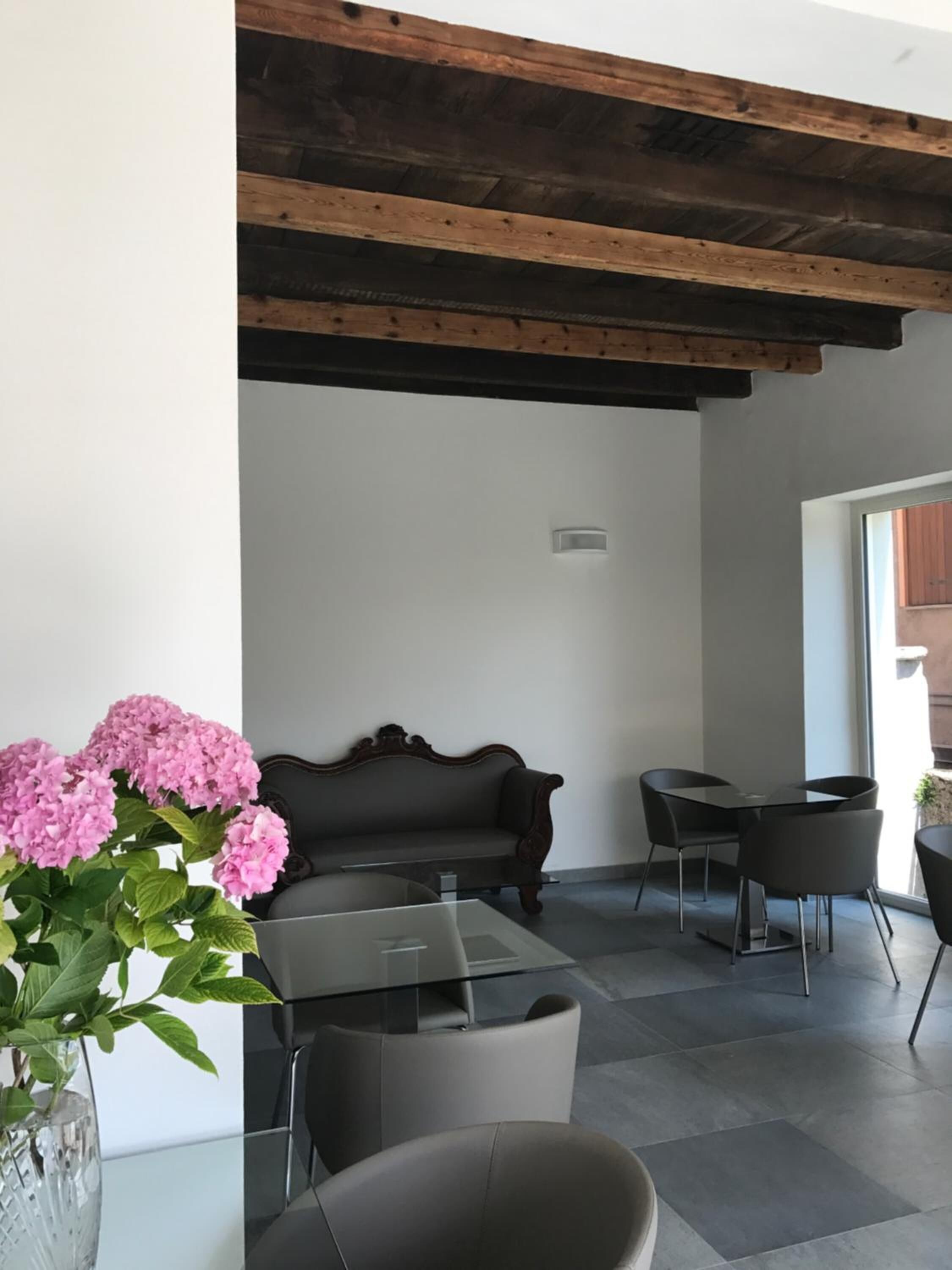 A modern interior with a dark leather sofa, a glass coffee table, and two chairs. There is a wooden ceiling and a potted plant with pink flowers.