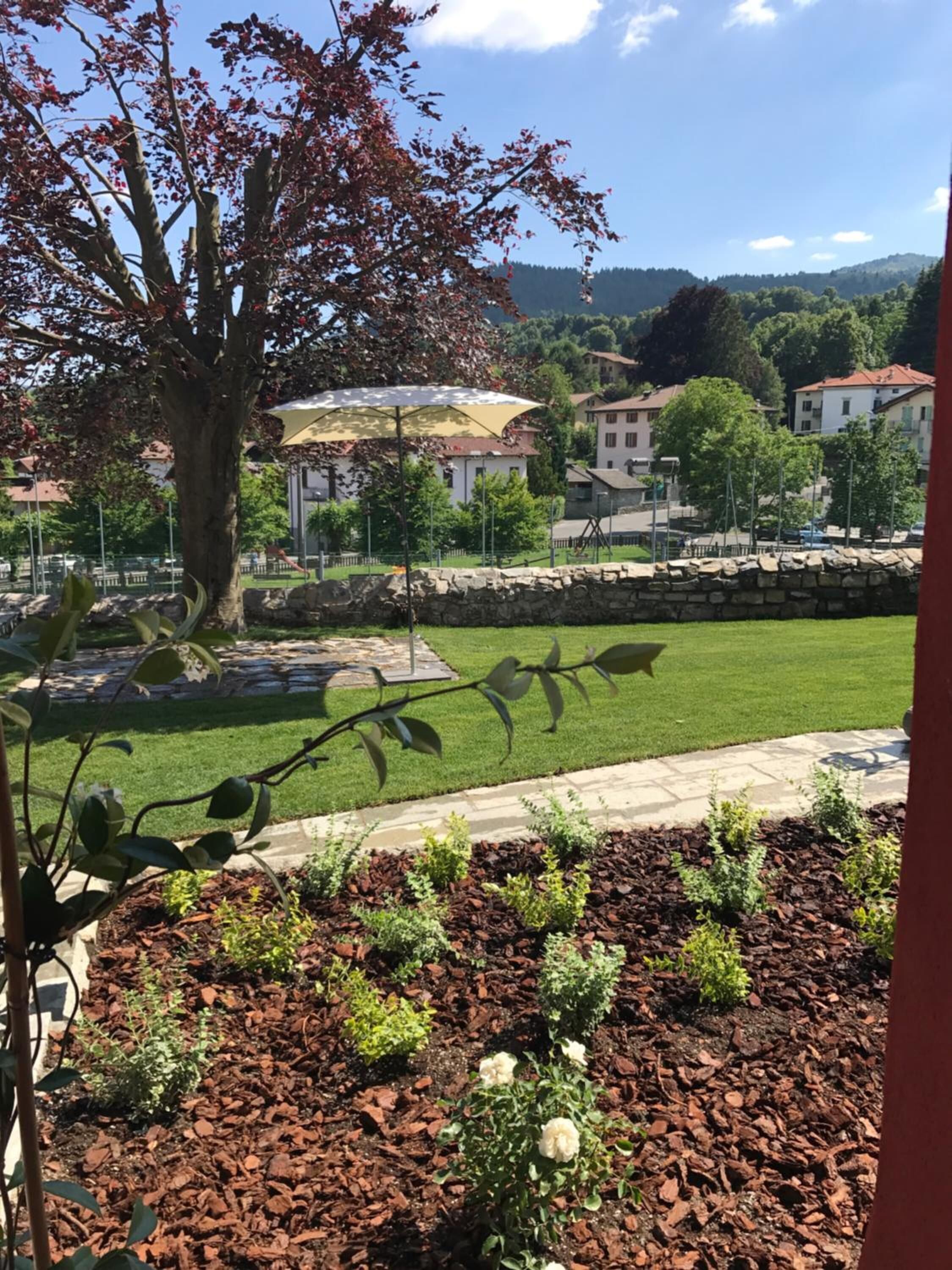 Un jardín ajardinado con un árbol, césped y un muro de piedra.