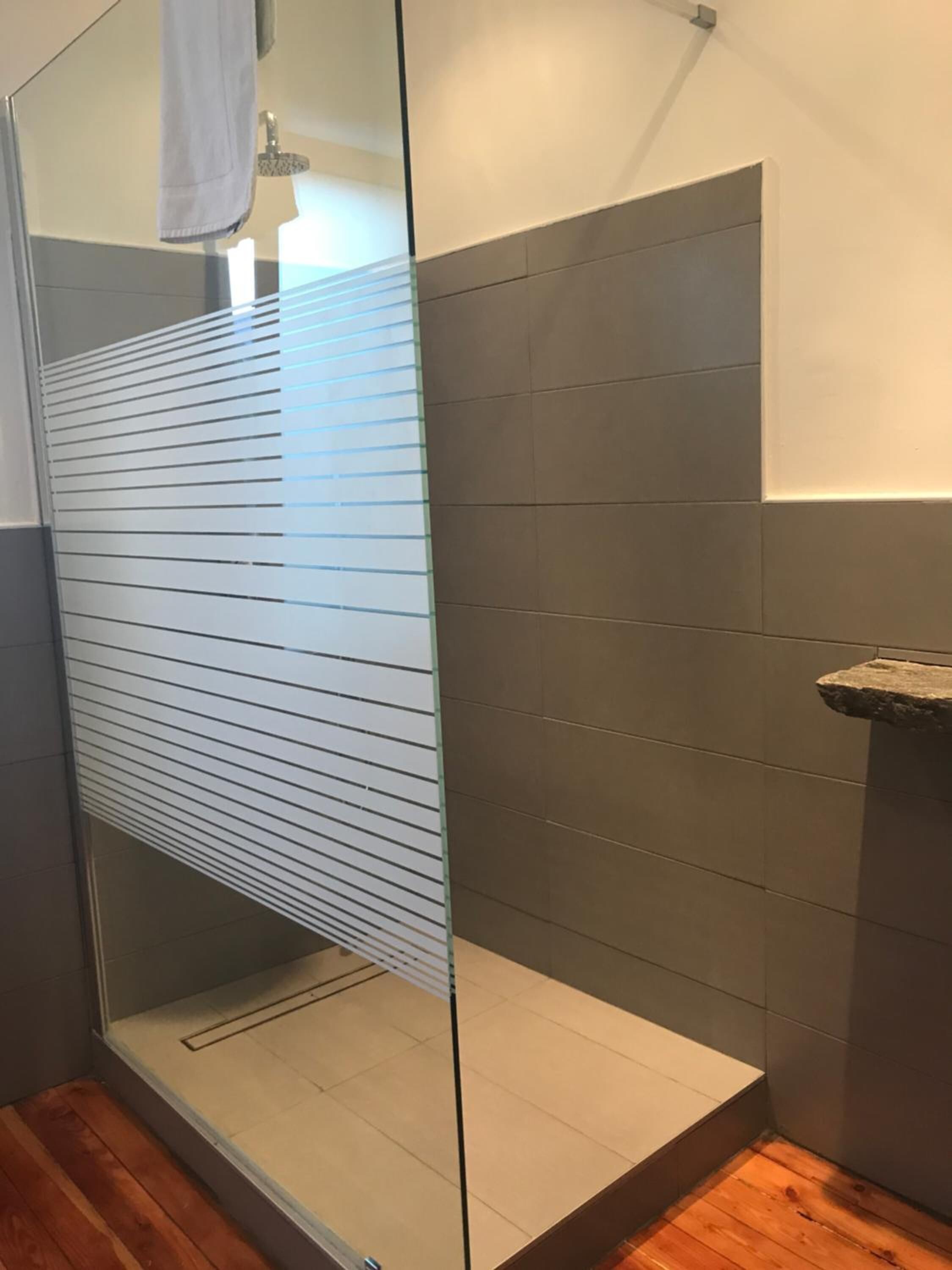 Une salle de bain moderne avec une douche à l’italienne en verre, un plancher en bois et des murs recouverts de carreaux gris.