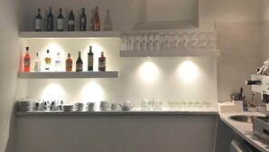 Zona de bar con estanterías llenas de botellas y vasos, una encimera de piedra y una cocina moderna con lavavajillas.