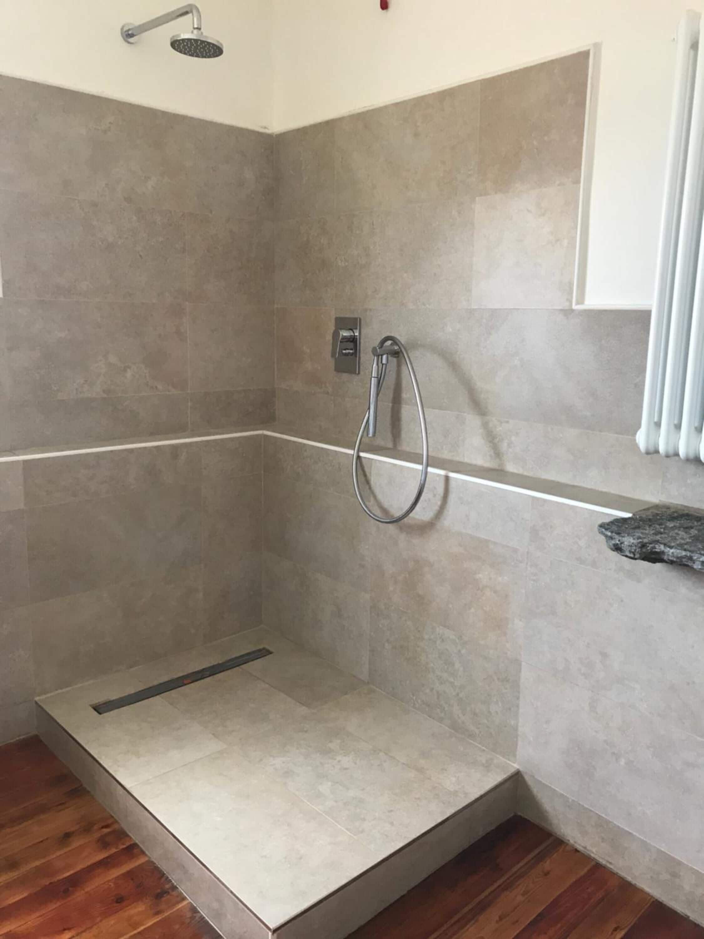 A shower area with a handheld showerhead, a wall-mounted control panel, and a tiled floor.