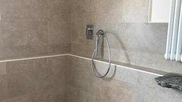 A shower area with a handheld showerhead, a wall-mounted control panel, and a tiled floor.
