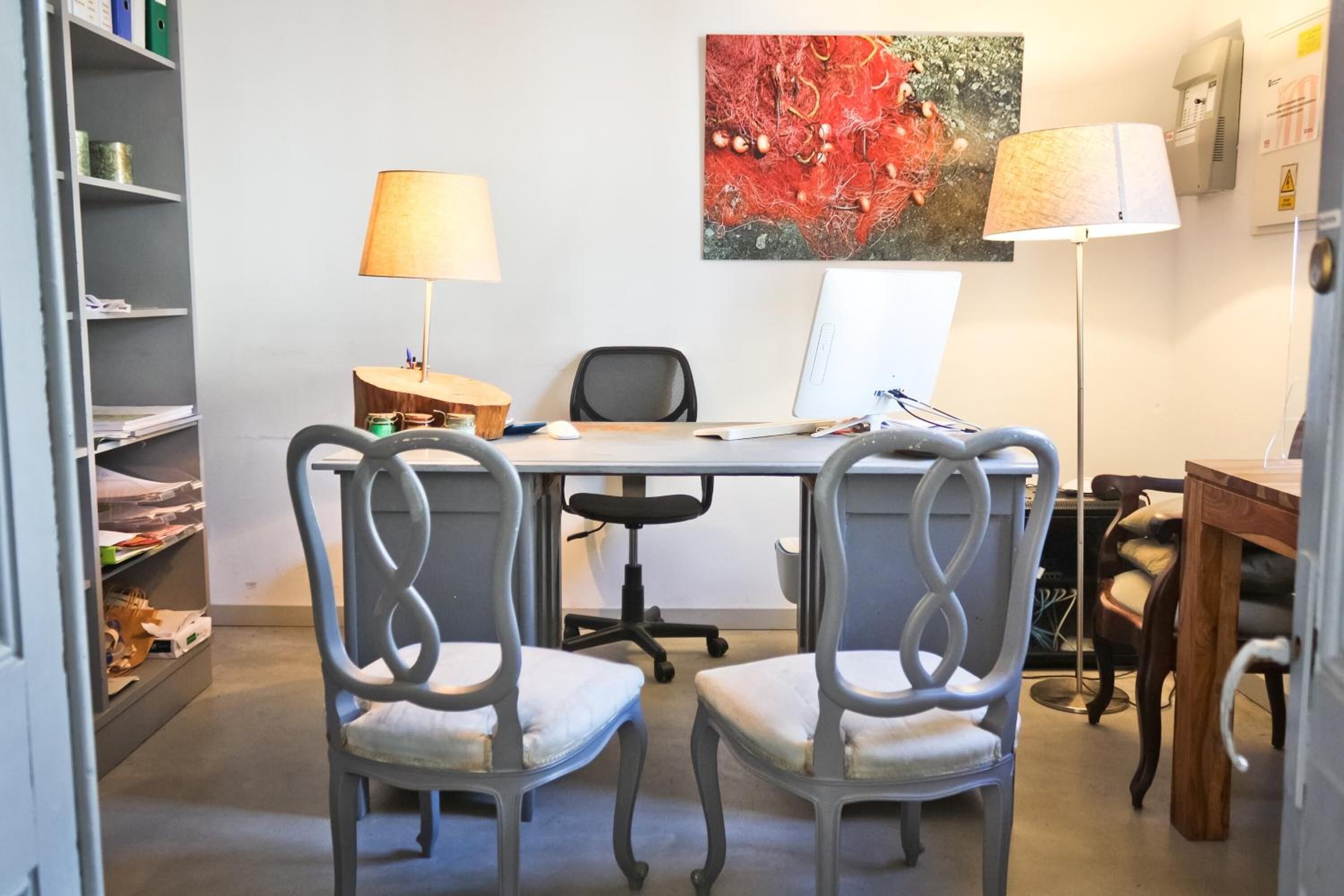 A room with a desk, two chairs, a computer, a lamp, and a bookshelf.