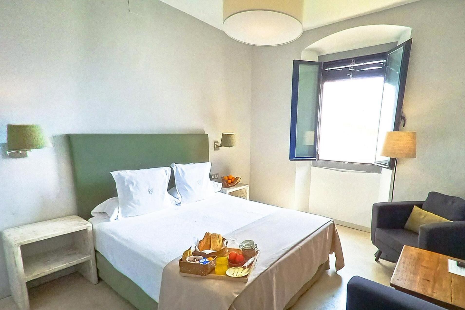 Een hotelkamer met een bed, nachtkastjes, een kleine zithoek en een raam met gordijnen.
