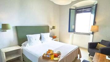Een hotelkamer met een bed, nachtkastjes, een kleine zithoek en een raam met gordijnen.