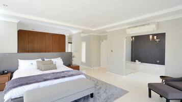 Ein modernes Schlafzimmer mit einem großen Bett, Nachttischen, einer Bank und einem Badezimmer mit Badewanne und Dusche.