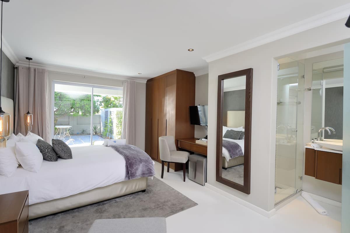 A modern hotel room with a large bed, a desk, a TV, and a glass shower area.