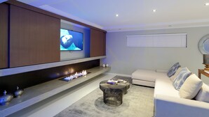 A modern living room with a flat-screen TV mounted on the wall, a fireplace with a glass front, a white sofa, and a round coffee table. - Grand Blue D (Cape Town)