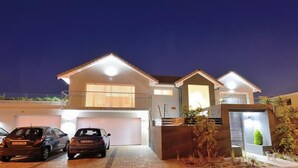 A modern two-story house with a garage, two cars parked in front, and a well-lit driveway. - Grand Blue D (Cape Town)