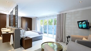 A modern hotel room with a large bed, a sitting area with a sofa and a coffee table, a TV mounted on the wall, and a balcony with curtains. - Grand Blue D (Cape Town)