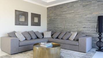 A modern living room with a grey sectional sofa, a round coffee table with books, and a textured stone wall.