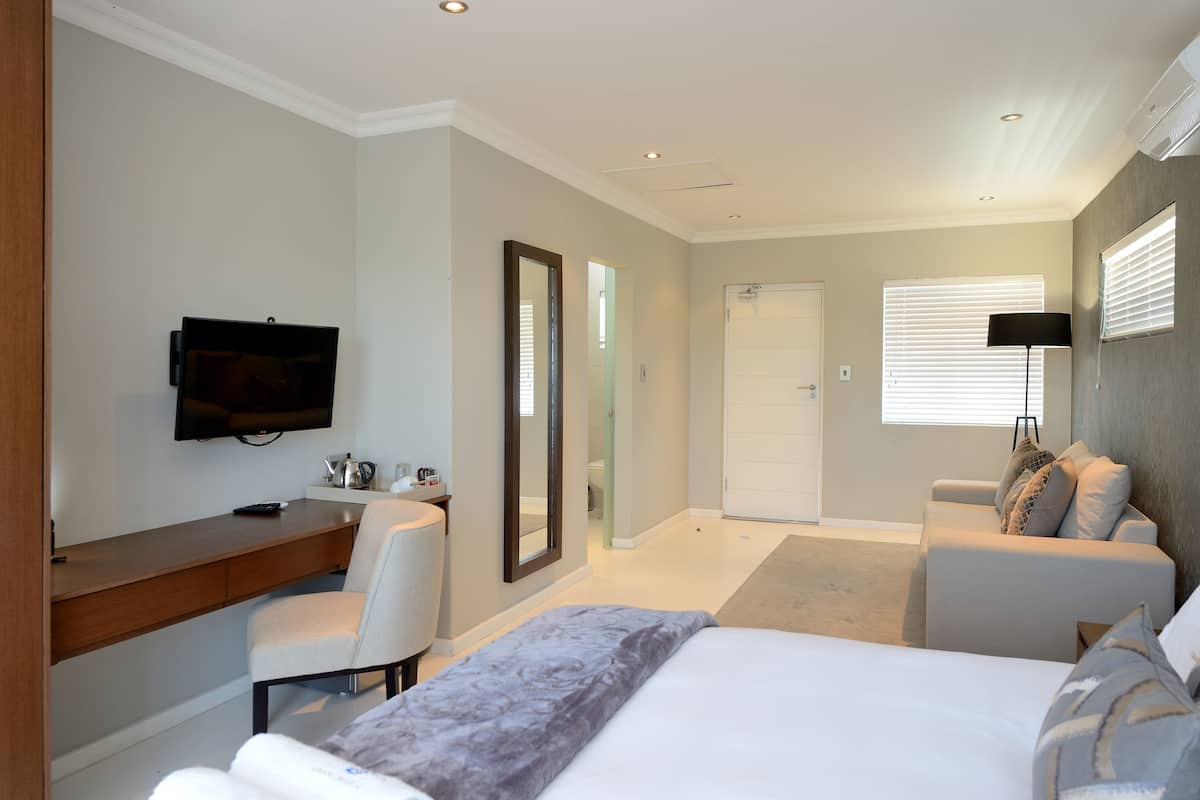 A modern hotel room with a bed, a desk, a chair, a television, and a sofa.