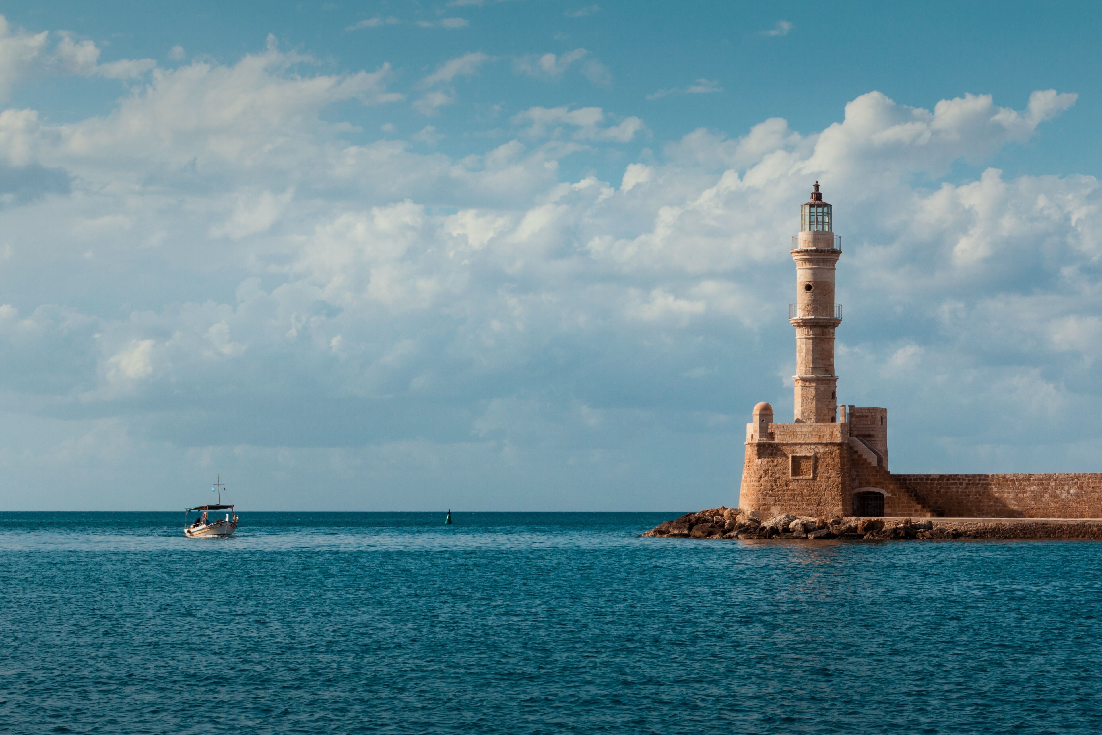 A lighthouse on a rocky outcrop with calm sea and a boat in the distance.