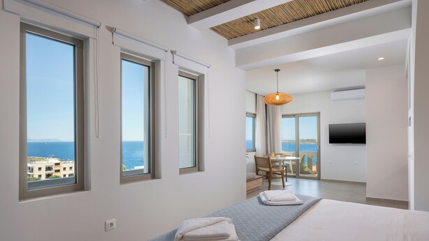 A modern hotel room with large windows, a balcony, a dining area, and a TV. - Esplanade Apartments (Chania)