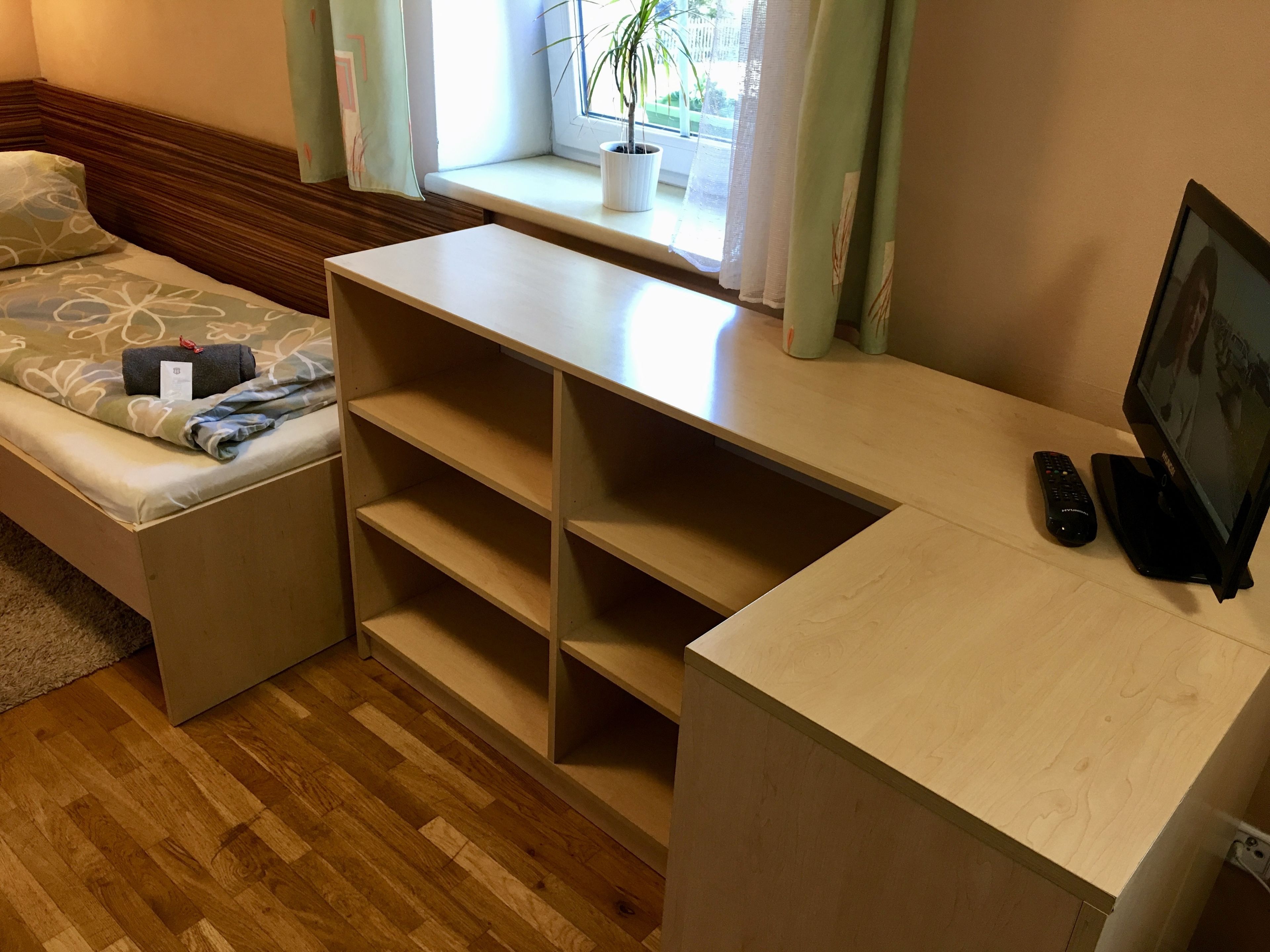 Una habitación con una cama, mueble empotrado con televisor, control remoto y una ventana con planta.