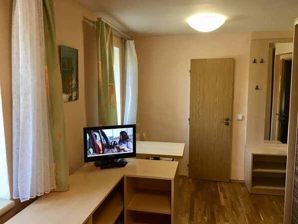 Una habitación con una televisión sobre una mesa de madera, una puerta y un espejo en la pared.