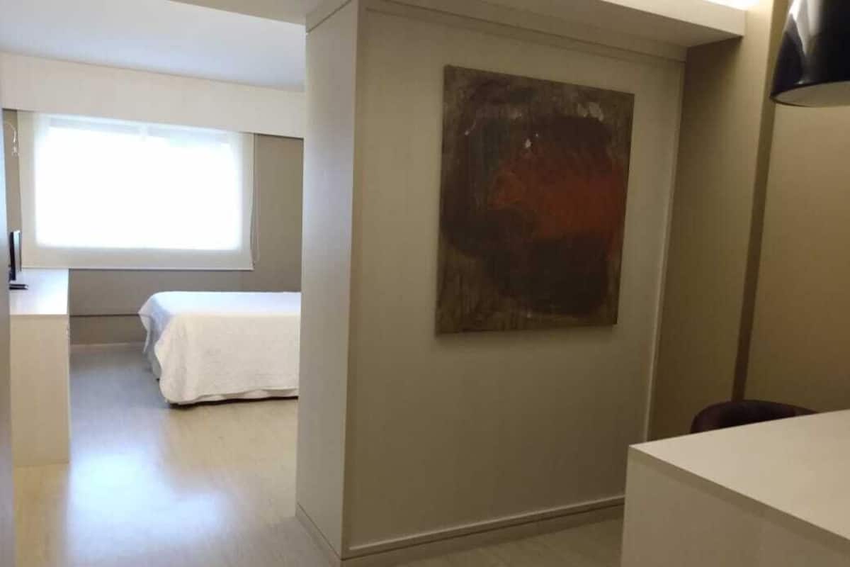 A hotel room with a bed, a desk, a chair, and a painting on the wall.