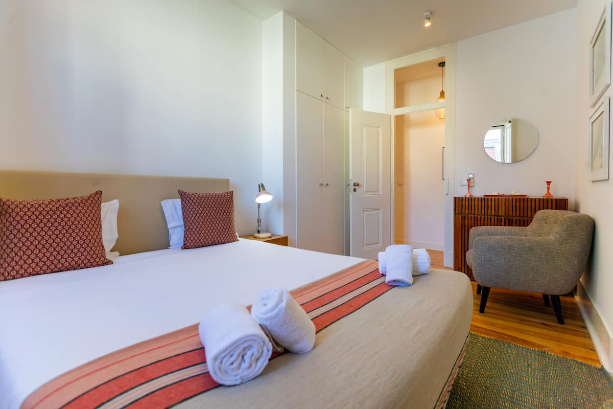 Ein Hotelzimmer mit einem großen Bett, einem Sessel, einem Schreibtisch und einem Spiegel an der Wand.