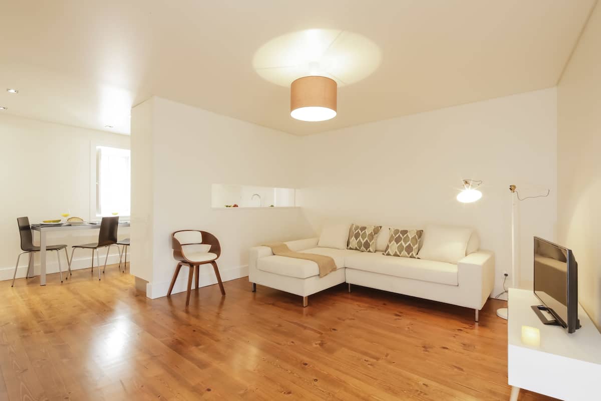 Ein modernes Wohnzimmer mit einem weißen Sofa, Holzboden und einem Essbereich mit Stühlen und Tisch.
