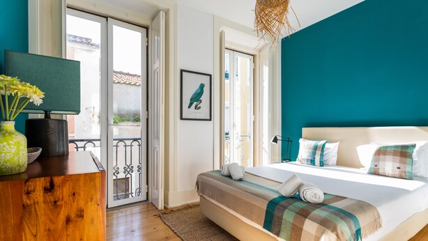 A bedroom with a bed, a wooden desk, a vase with flowers, and a framed picture on the wall.