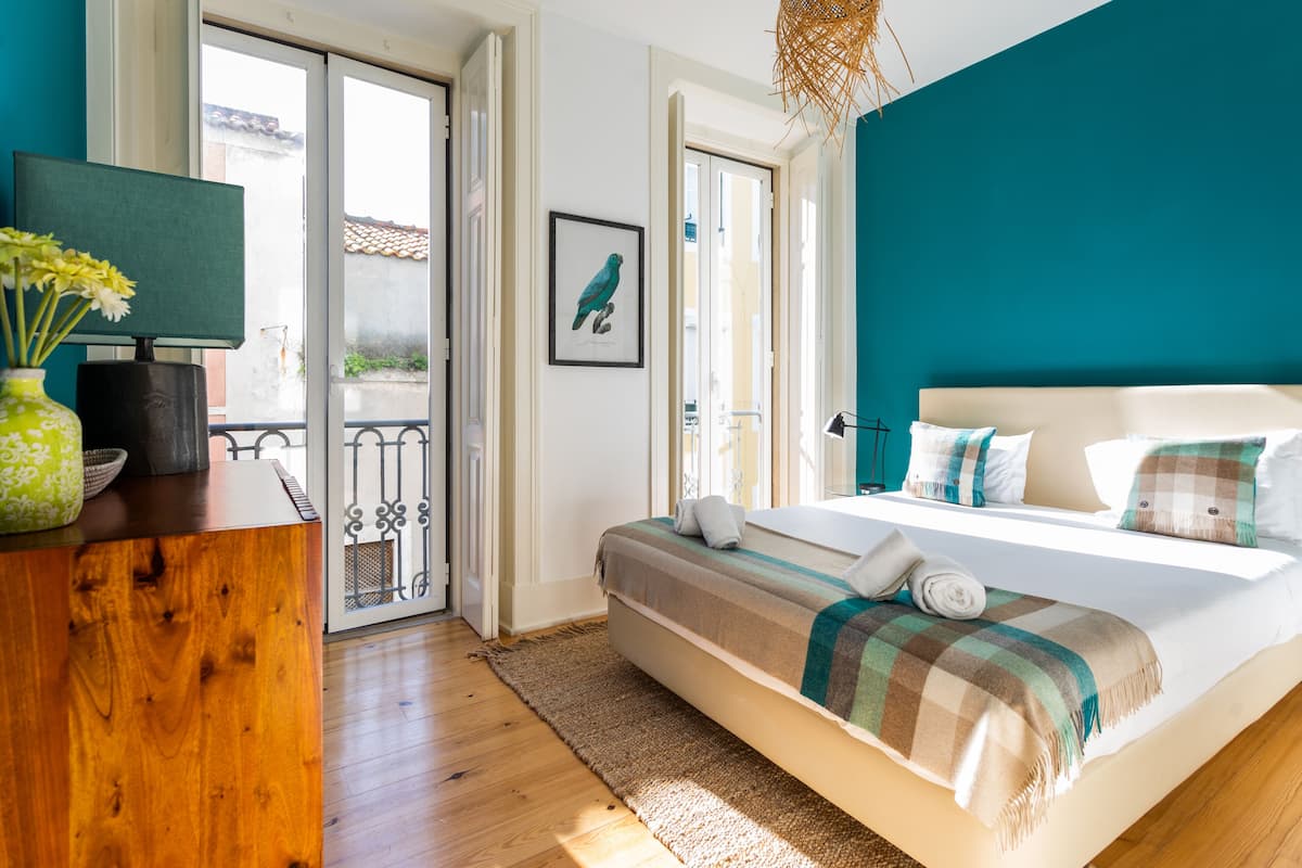 Ein Schlafzimmer mit einem Bett, einem Holztisch, einer Blumenvase und einem gerahmten Bild an der Wand.
