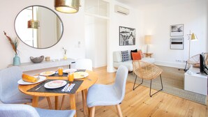 A modern living room with a dining area, featuring a round table, chairs, a sofa, and a large mirror.
