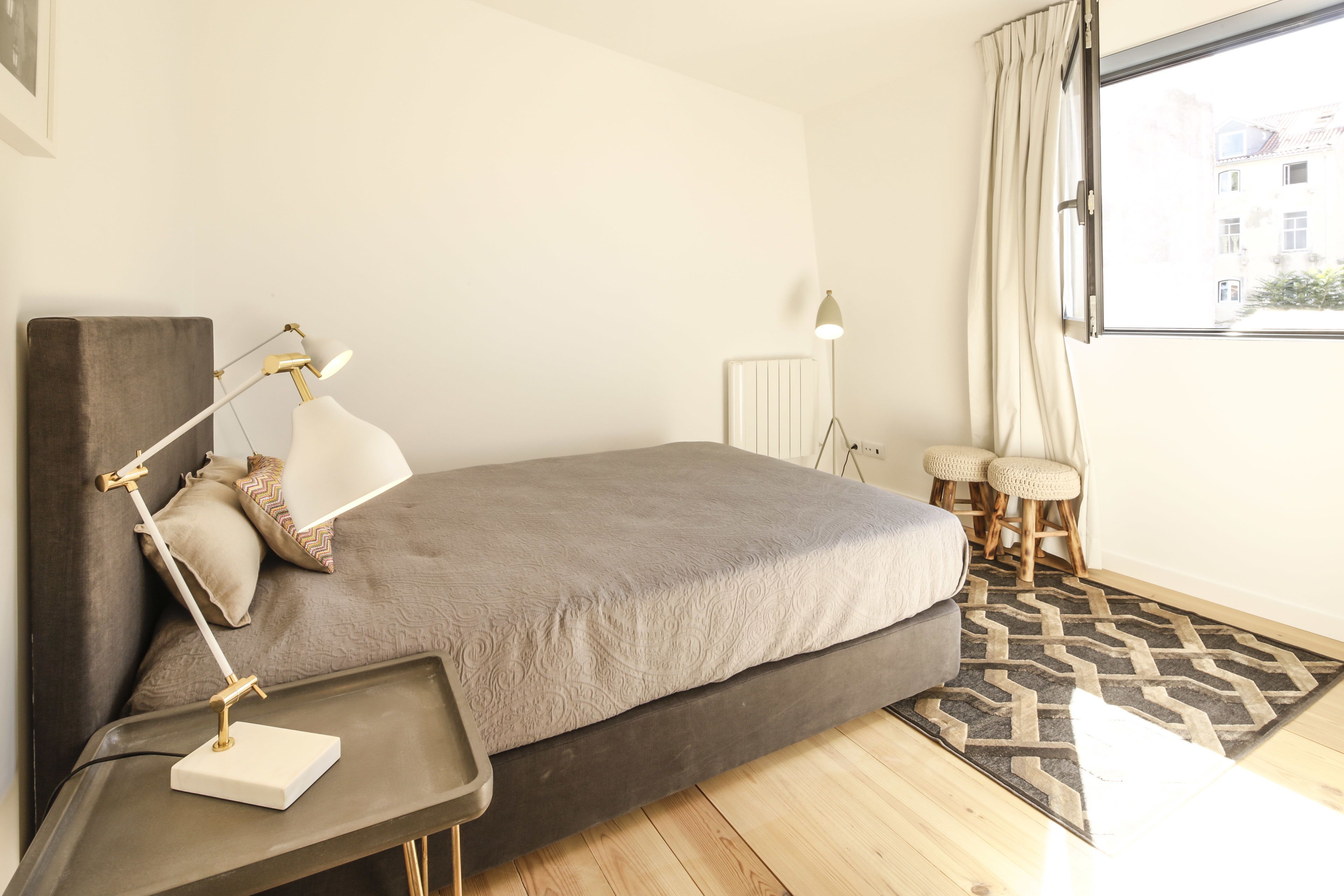 A modern bedroom with a bed, bedside table, lamp, and a view of the outside through a window.