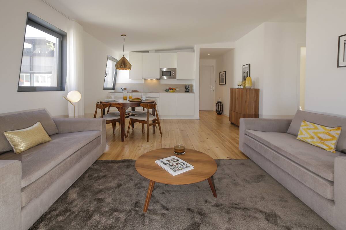 A modern living room with a grey sofa, a coffee table, and a dining area with a wooden table and chairs.