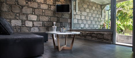 A modern living room with a stone wall, a flat-screen TV, a round table, and a dark-colored sofa.