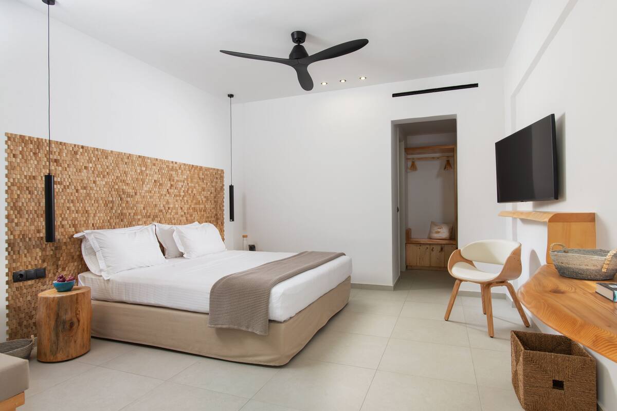 Un dormitorio moderno con cama, ventilador de techo, televisor y panel de pared de madera.