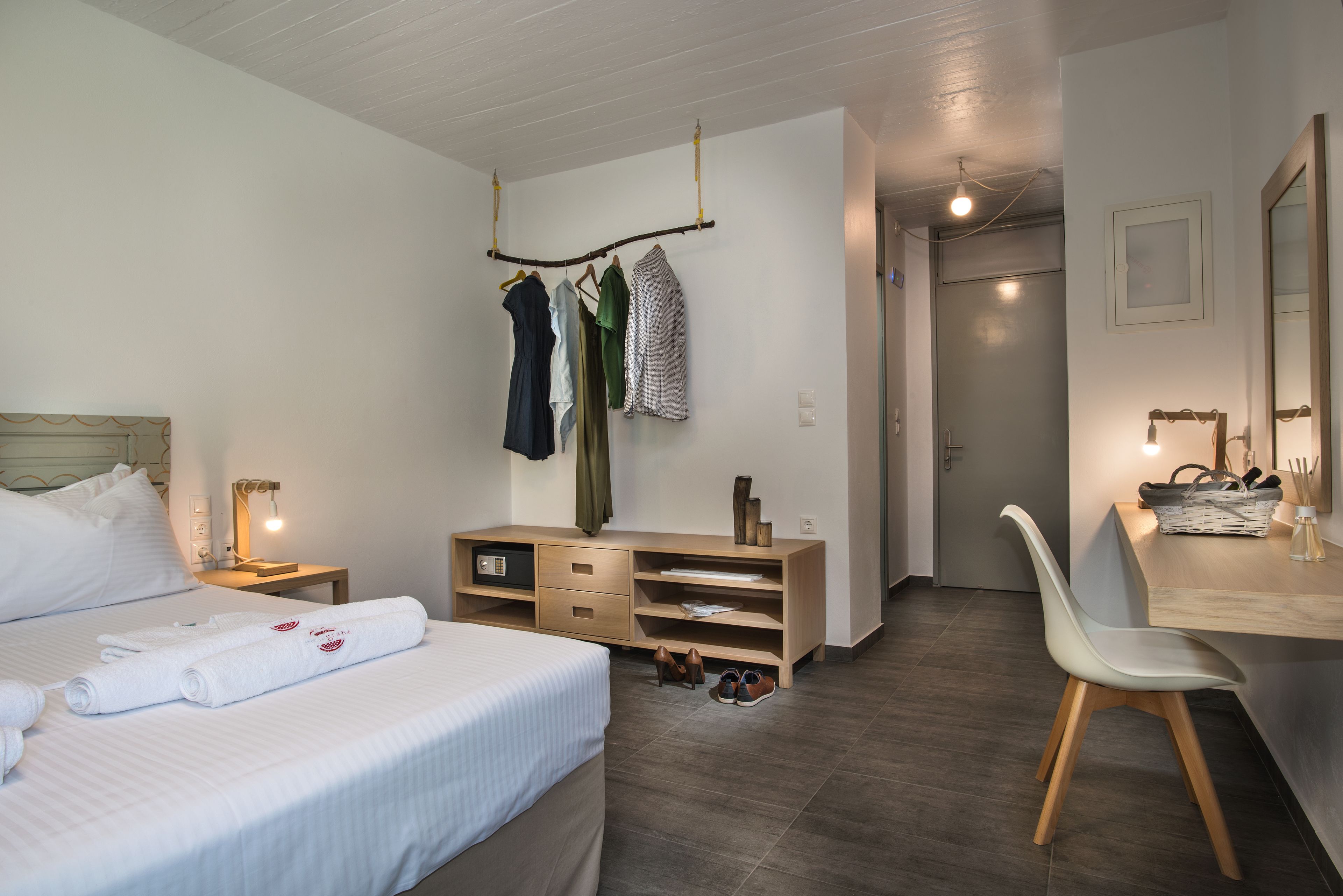 A bedroom with a bed, bedside tables, a desk with a chair, a wardrobe, and a hanging clothes rack.