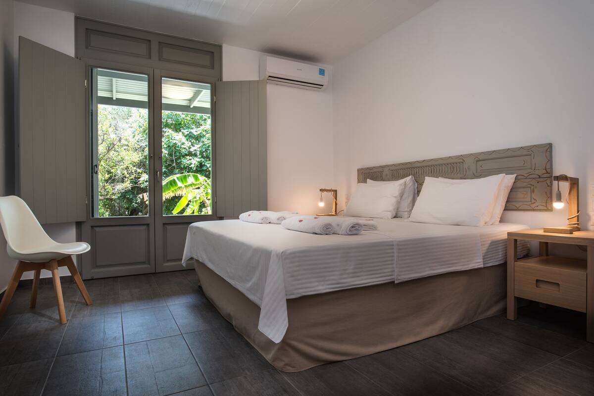 Un dormitorio con cama, mesita de noche, silla y ventana con vistas a zonas verdes.
