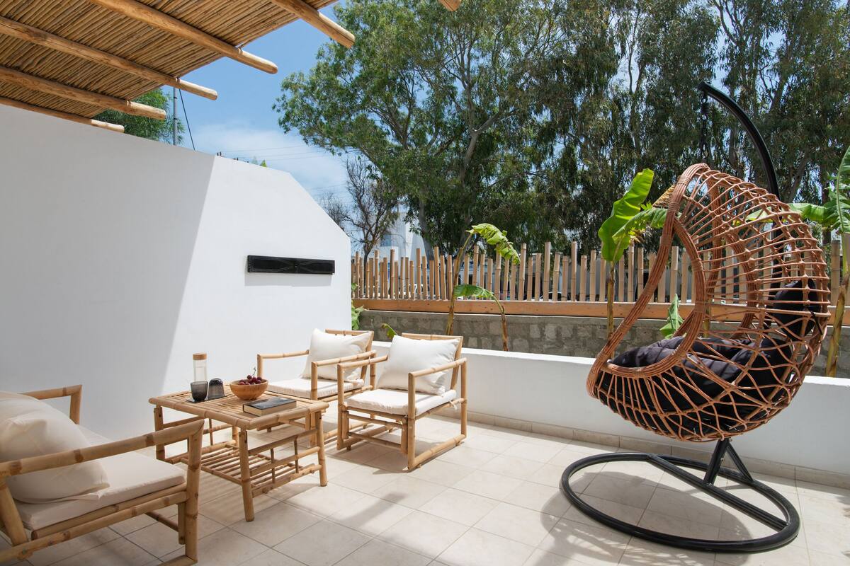 Un patio con muebles de mimbre, una silla colgante y vistas a árboles.