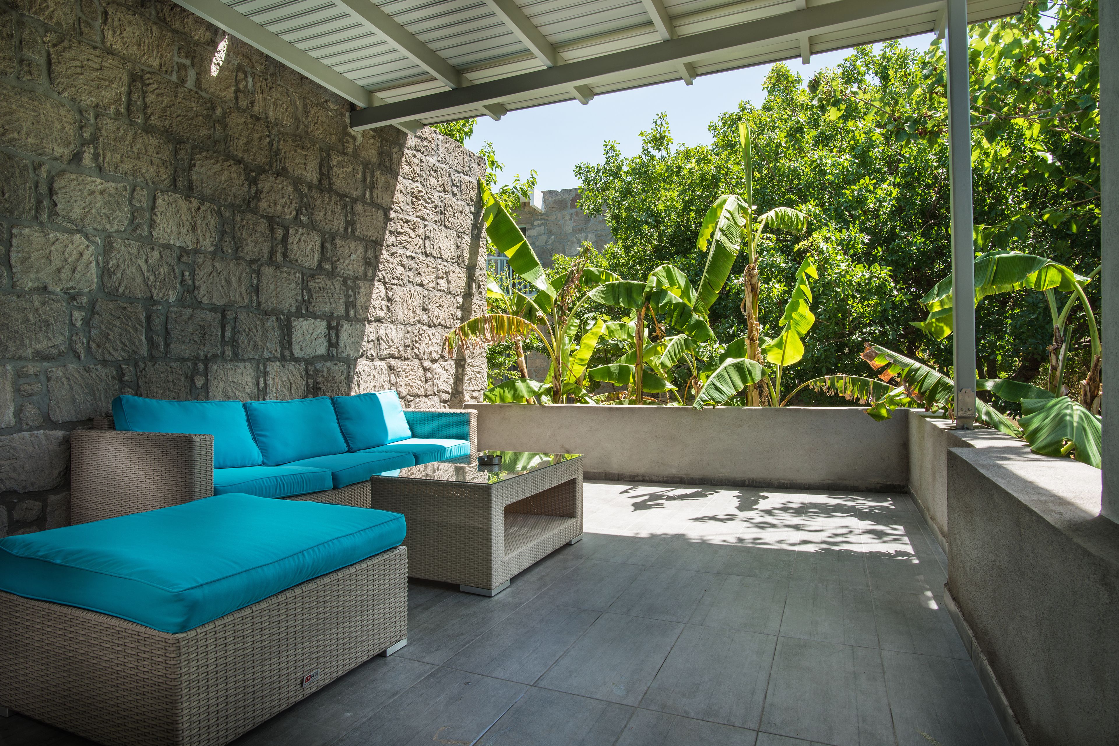 A covered outdoor seating area with wicker furniture and a stone wall.
