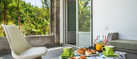 A balcony with a table set for breakfast, including croissants, pizza, and a drink.