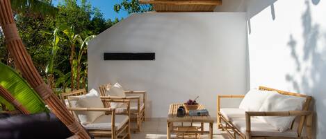 Un área de estar moderna al aire libre con mobiliario de mimbre y una pared blanca.
