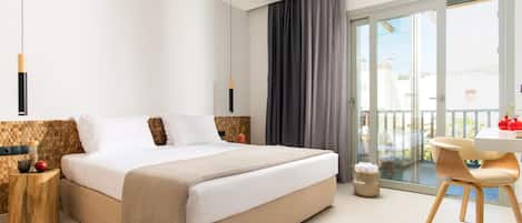 Habitación de hotel moderna con una cama grande, una zona de comedor con mesa y sillas, y un balcón con vistas.