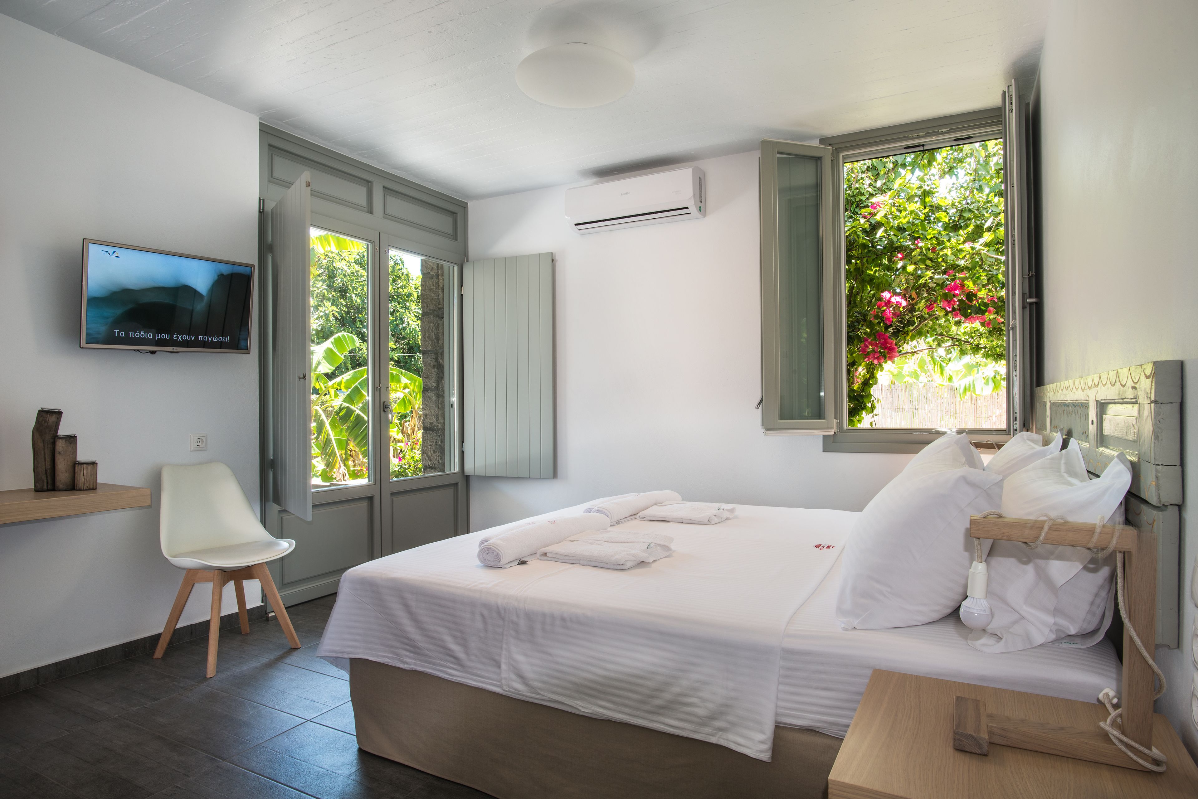 Un dormitorio con una cama, una silla, un televisor y una ventana con vistas a la vegetación.