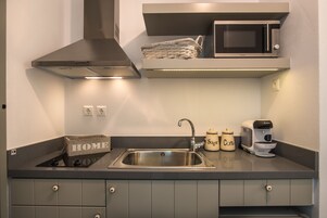 Uma cozinha moderna com uma pia de aço inoxidável, um micro-ondas, uma cafeteira e uma cesta sobre o balcão.