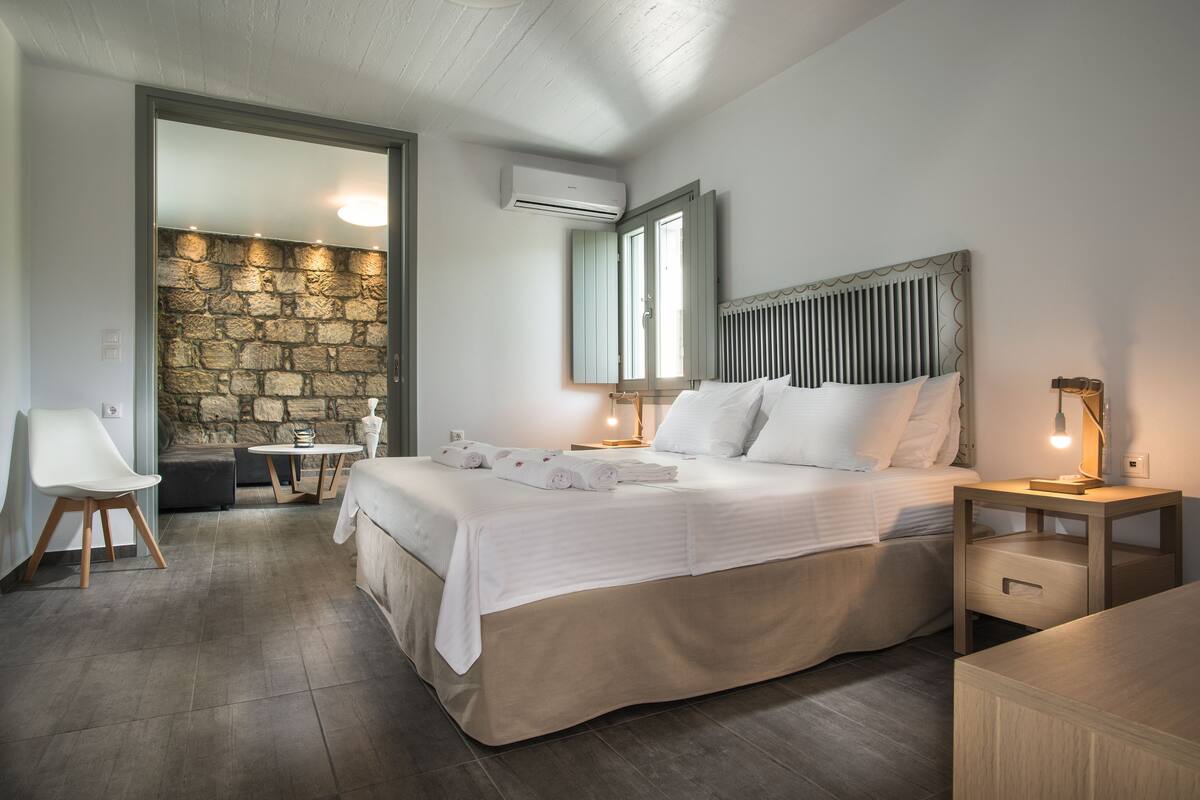 Un dormitorio con cama, mesitas de noche, escritorio, una silla y pared de piedra.