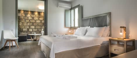 A bedroom with a bed, bedside tables, a desk, a chair, and a stone wall.