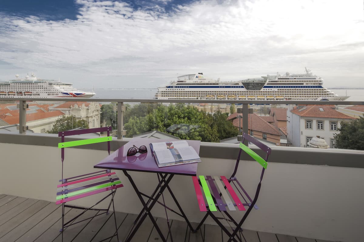 A balcony with a table and chairs, overlooking a waterfront with cruise ships.