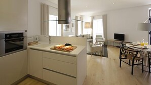 Une cuisine moderne dotée d’un îlot central, un coin repas avec une table ronde et un espace de vie comprenant un canapé et un téléviseur.