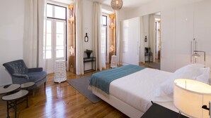 Ein modernes Schlafzimmer mit einem großen Bett, einem Sessel, einem kleinen Tisch und einer Lampe.