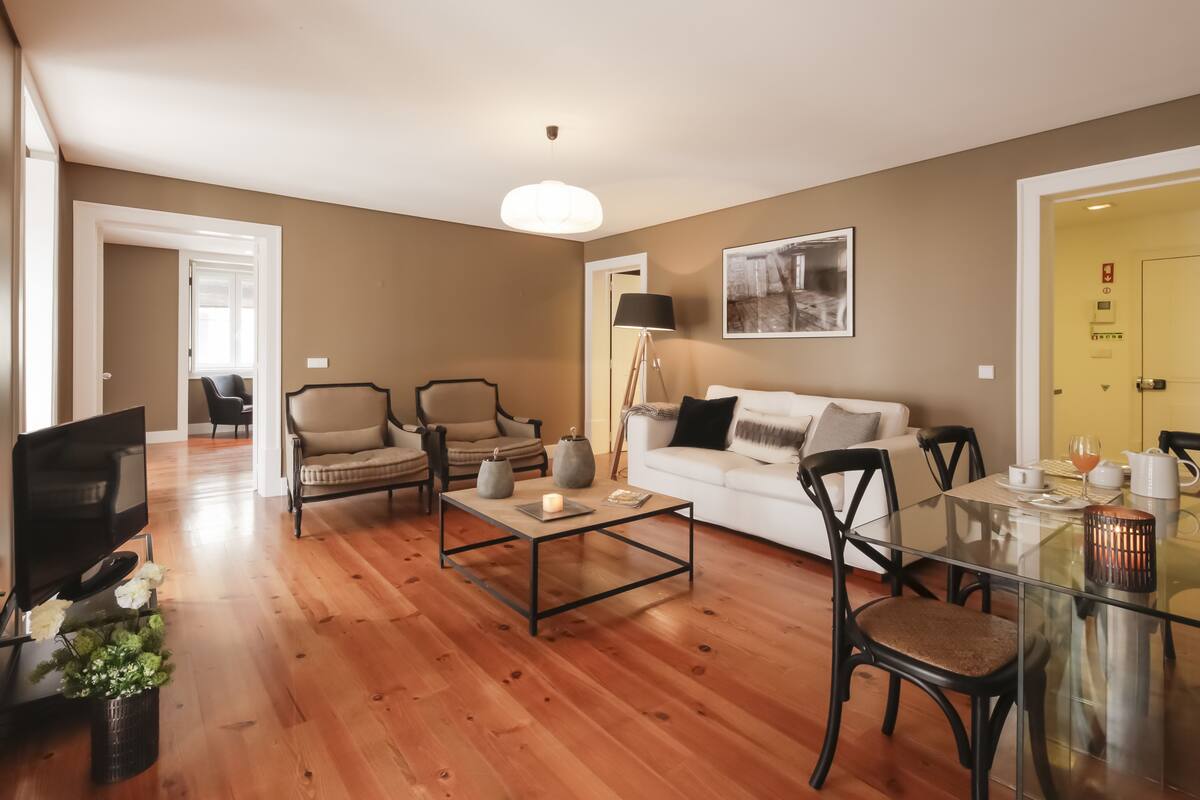 A modern living room with a glass coffee table, two sofas, a TV, and a dining table with chairs.