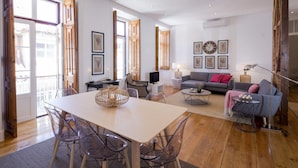 Ein geräumiges Wohnzimmer mit einem großen Holztisch, klaren Stühlen, einem grauen Sofa und einem Couchtisch.