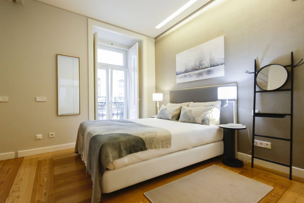 A bedroom with a large bed, bedside lamps, a mirror, and a painting on the wall.